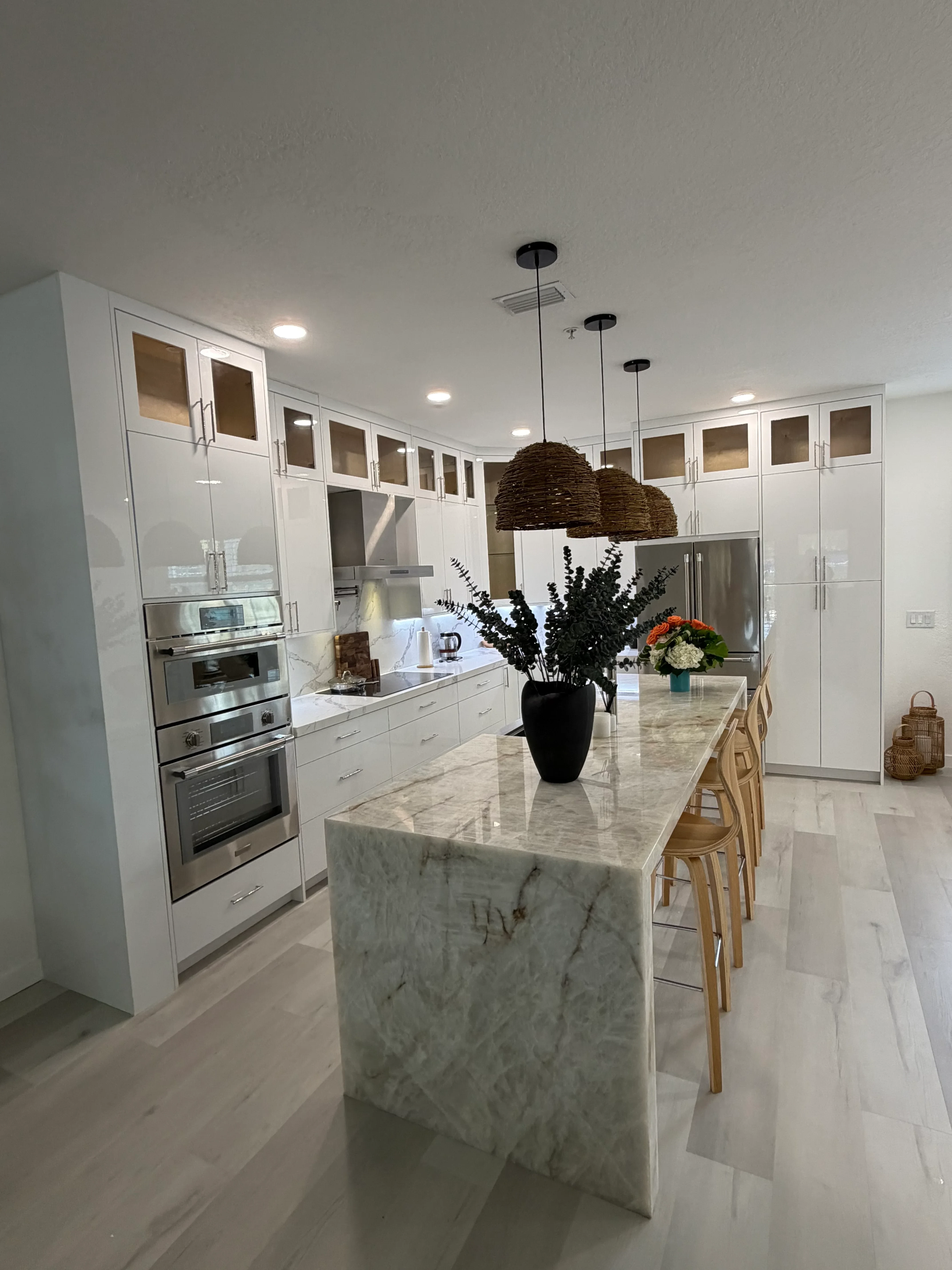 White custom cabinetry with glass doors, marble waterfall island, and stainless steel appliances