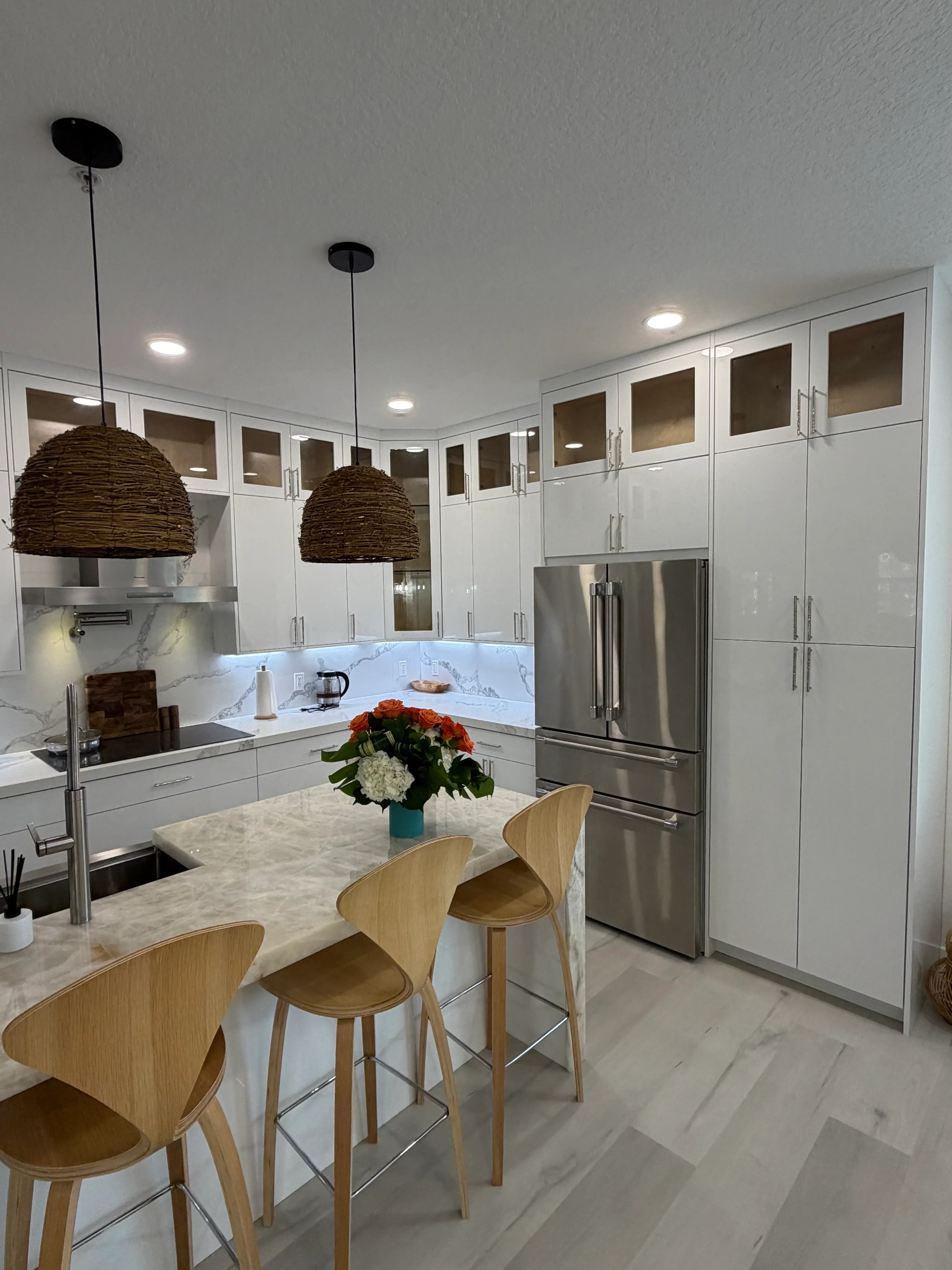 White lacquered cabinetry, marble countertop, stainless steel appliances, and glass-front cabinets in modern kitchen